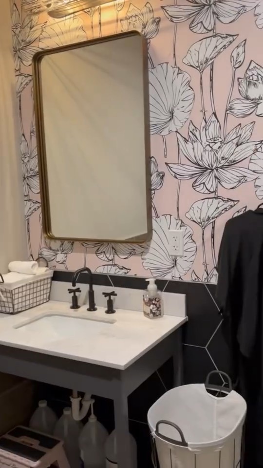 Restroom with blush botanical wallpaper, brass mirror and white vanity