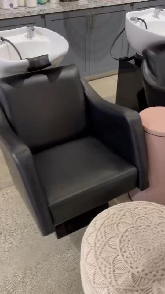 Black leather backwash shampoo chair in front of white bowls and gray cabinets