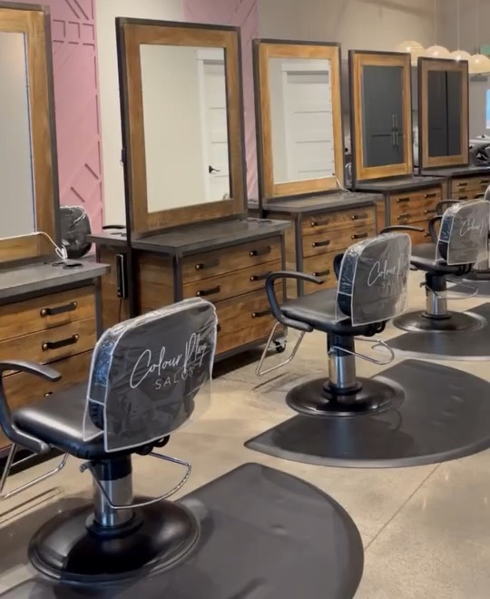 Wood-and-steel styling stations with Colour Play branded chair covers on polished concrete